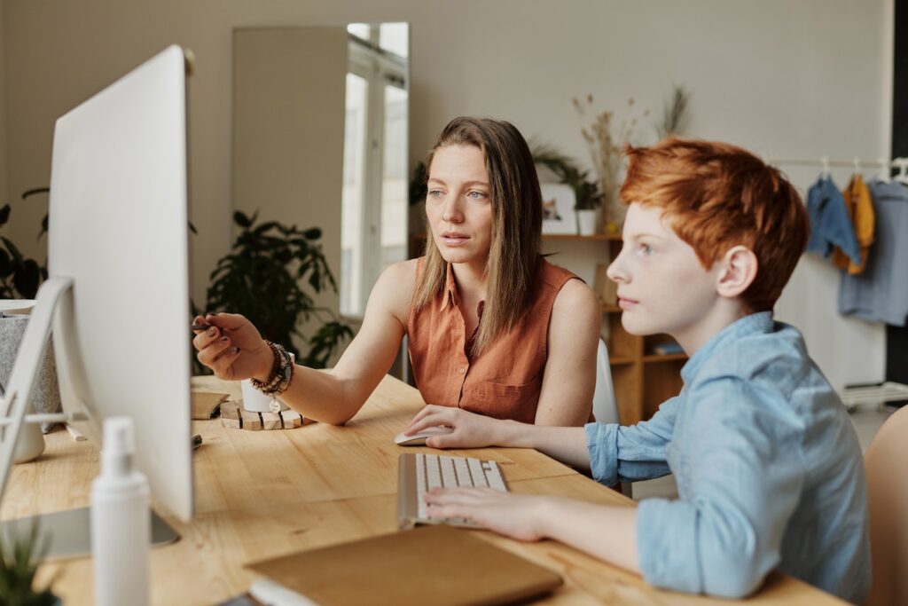 Adult sitting beside a boy and guiding him through an activity at a desk