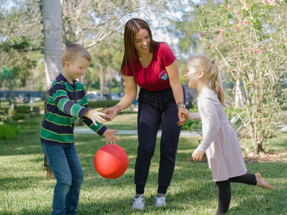 ABA therapist playing with two children outdoors, using play-based learning to build social and communication skills.