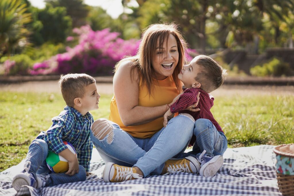 Mother playing with her two young sons on a picnic blanket at the park