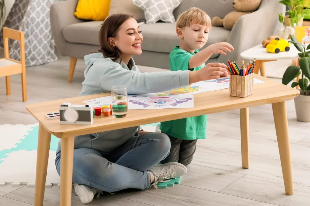 Young woman and little boy drawing with markers at a living room table