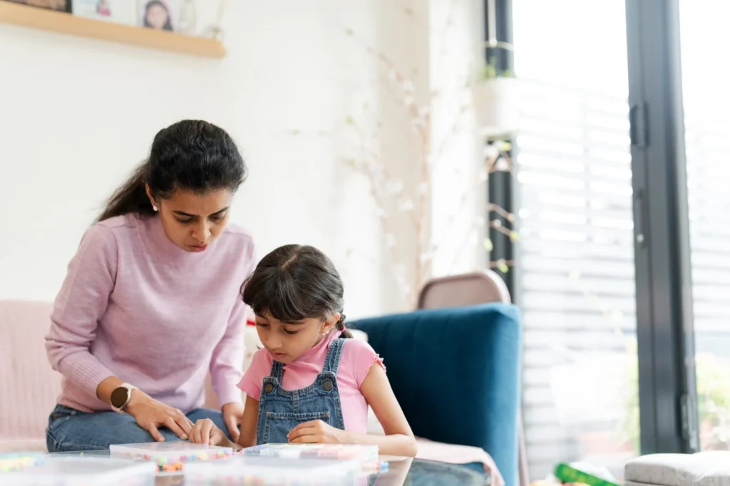 Mother and young daughter working on a bead craft together at the living room table