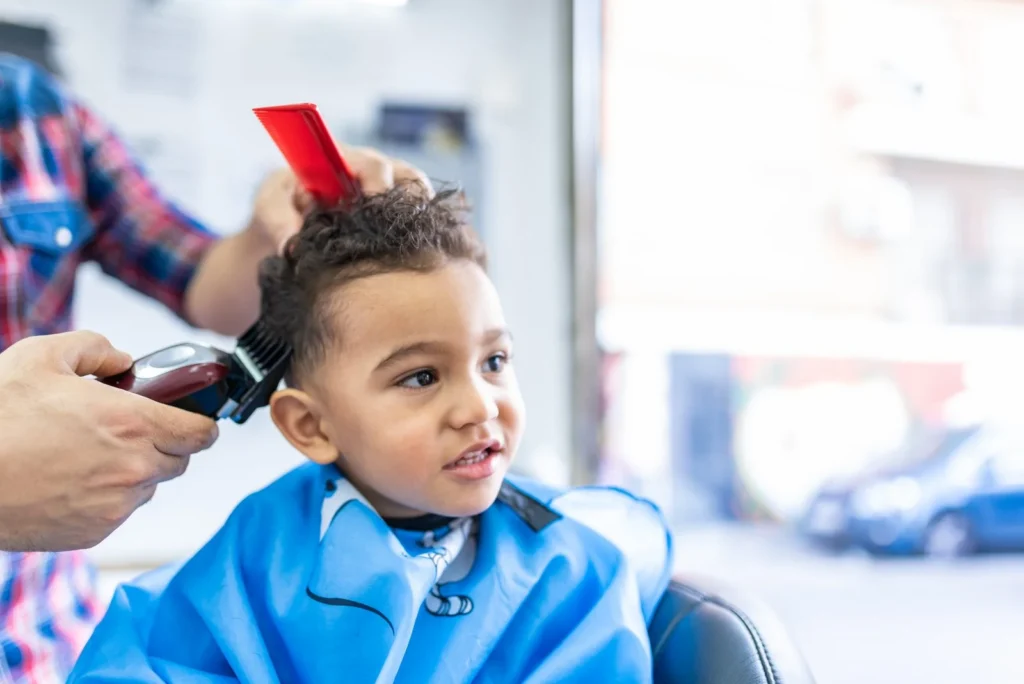 Little boy in a blue cape sitting calmly for a haircut at a barbershop