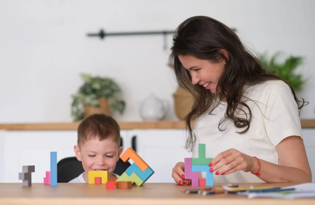 Woman and young boy building with colorful puzzle blocks at a table at home