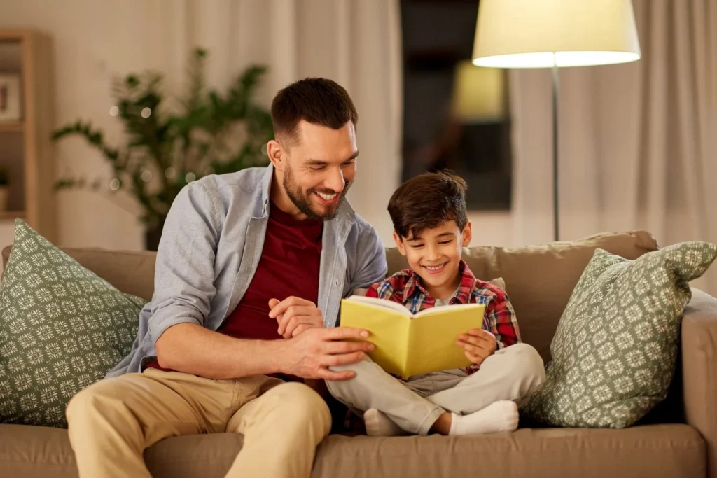 Father reading a picture book with his young son on the living room sofa