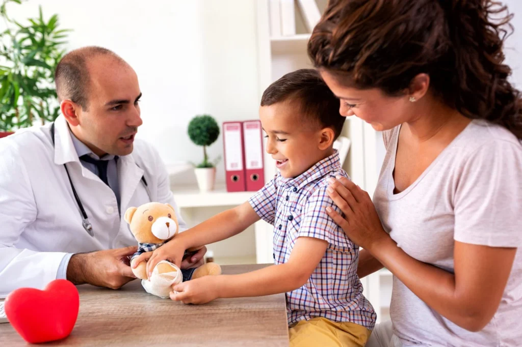 Young boy holding a teddy bear at a doctor's appointment with his mother beside him