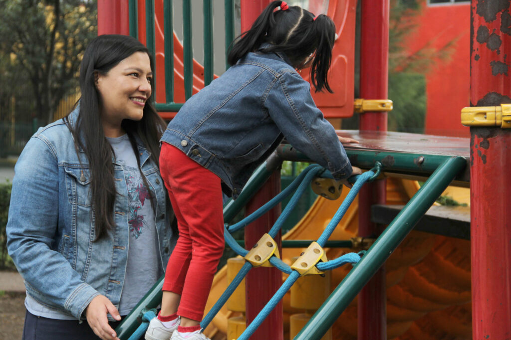 Mother helping her daughter climb playground equipment at a park