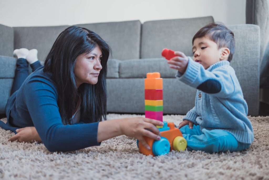 Mother and toddler stacking blocks together on the living room floor