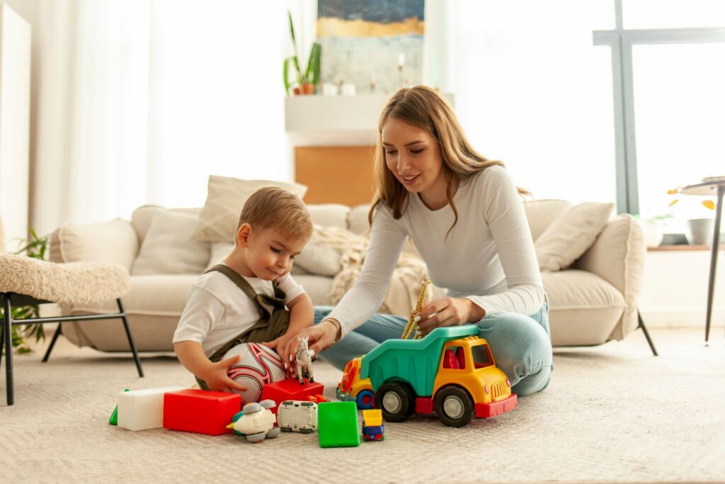 Therapist playing with a toddler and a toy truck on the living room floor